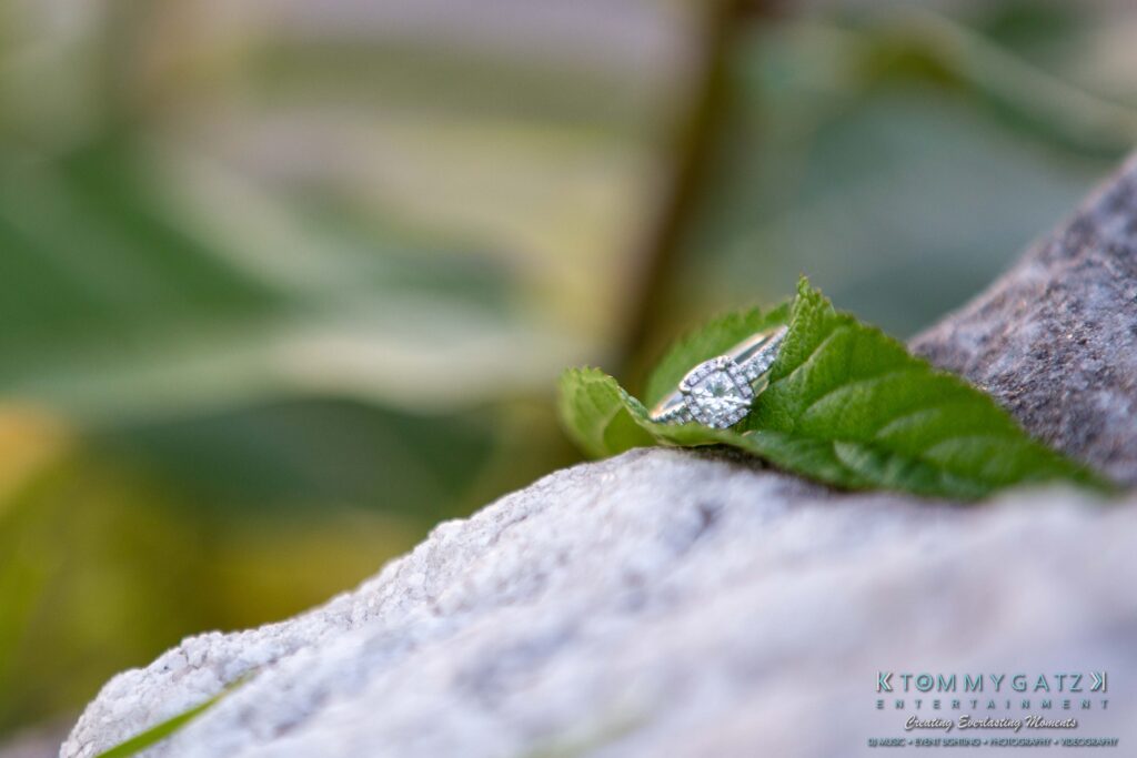 Diamond engagement ring on a green leaf over a rock, with a blurred natural background.