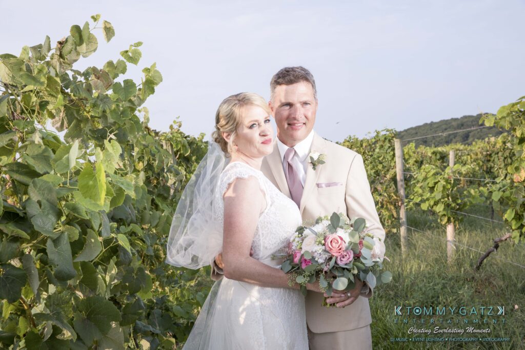 Bride and groom pose together in a vineyard; the bride holds a bouquet.