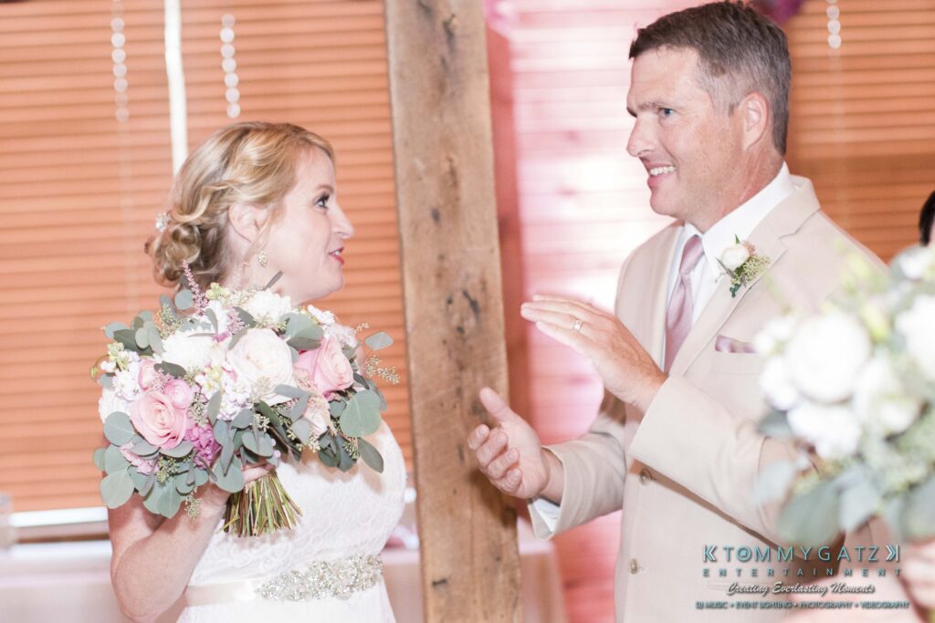 A bride holding a bouquet converses with a groom in a light suit at an indoor venue.