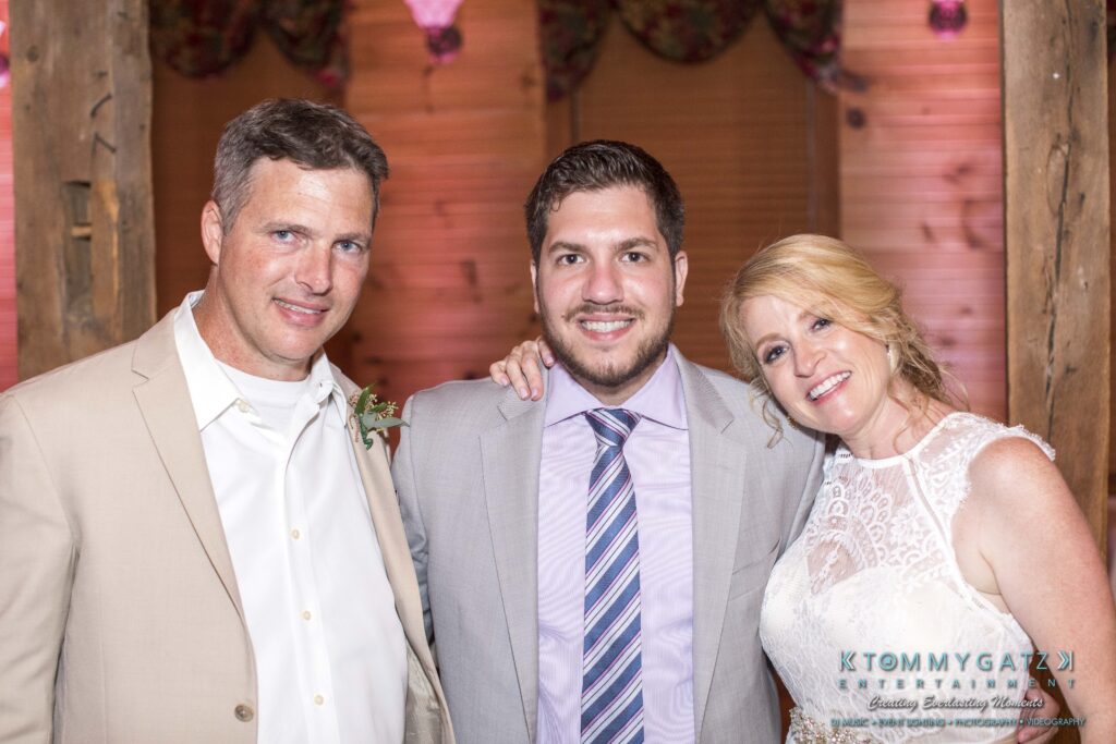 Three people dressed formally, two men and a woman, smiling and posing together indoors.