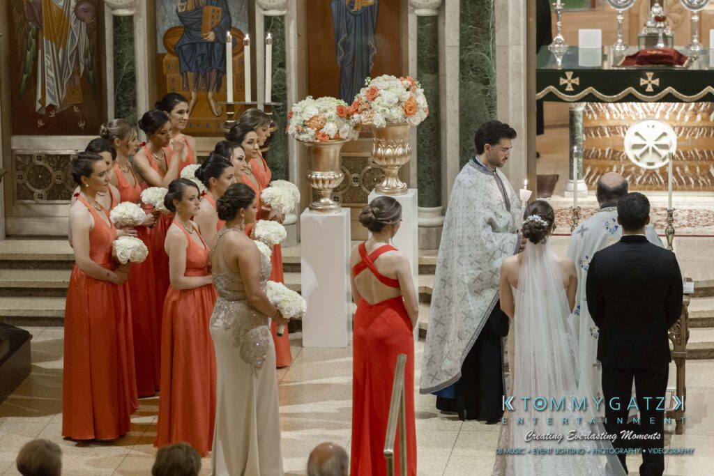 A formal ceremony in a church with bridesmaids in red dresses holding bouquets, a priest in a white robe, and a couple standing near the altar.
