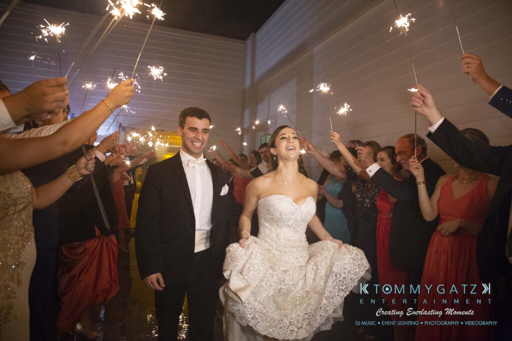 A bride and groom smile while walking through a crowd of people holding sparklers at night.